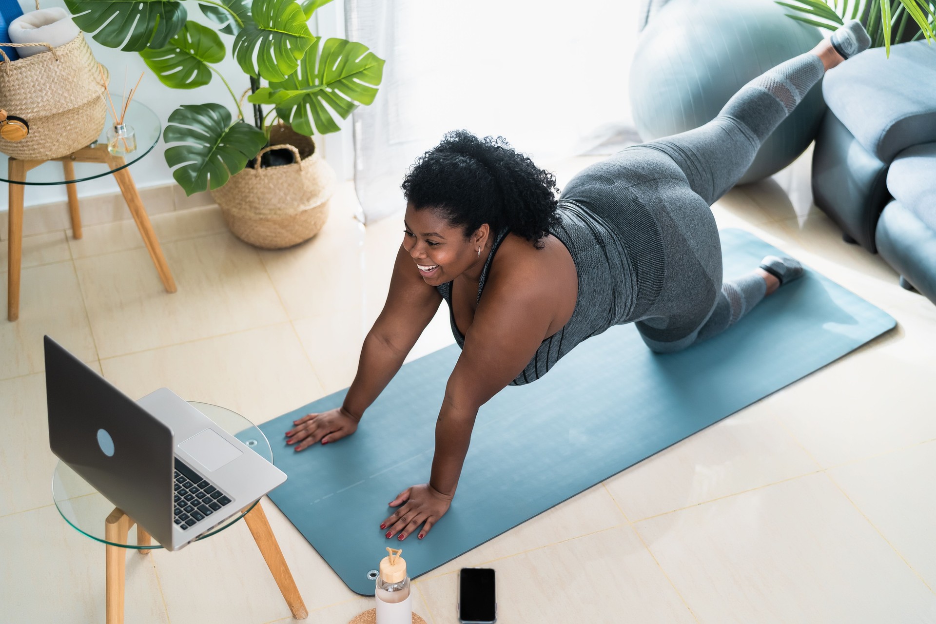 Young African curvy woman doing pilates virtual fitness class with laptop at home - Sport wellness people lifestyle concept